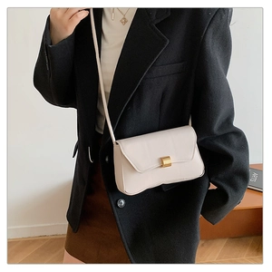 Detail of minimalist cream crossbody bag with gold magnetic buckle on female model