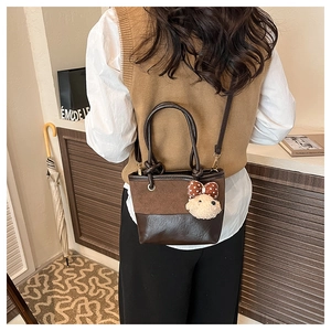 Close-up of brown two-tone crossbody tote bag with cute teddy bear charm on the side
