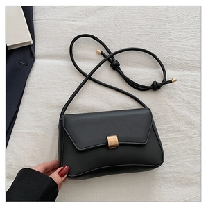 Detail of minimalist black matte leather bag with golden buckle on white fabric