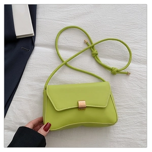 Detail of neon green leather shoulder bag with gold square buckle on white fabric
