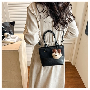 Detail of black crossbody bucket bag with teddy bear charm in a lifestyle setting