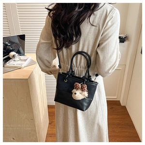 Detail of black suede patchwork bucket bag featuring a teddy bear charm and sleek strap