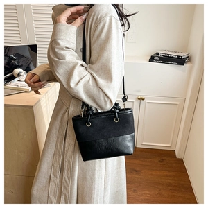 Detail of black bucket bag with mixed textures styled on model wearing a beige dress