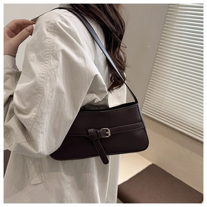 Close-up of glossy chocolate brown shoulder bag with buckle detail on female model