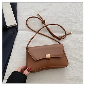 Detail of minimalist brown baguette bag featuring a gold square buckle and cord strap