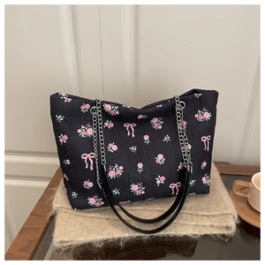 Close-up of black floral tote bag with textured fabric, pink roses and chain strap