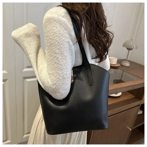 Minimalist black matte leather tote bag shown on shoulder in a warm interior scene