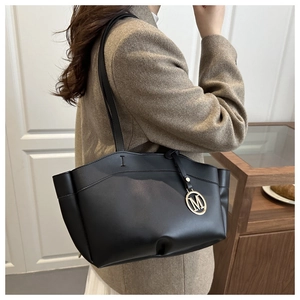 Detail of black leather tote bag with gold metal M charm and elegant shoulder strap
