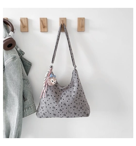 Détail du sac fourre-tout gris à motifs nœuds avec breloque ours en peluche sur le mur