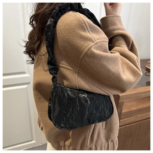 Detail of black pleated shoulder bag with silver bow emblem on a camel wool coat