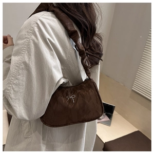 Brown pleated underarm bag with silver bow detail worn by model in minimalist setting