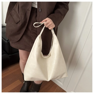 Detailed texture of a cream-colored leather tote bag held by a model in a brown suit