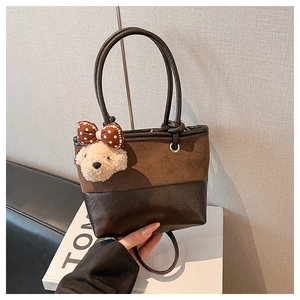 Detail of brown contrast material handbag featuring a cute plush bear charm with bow
