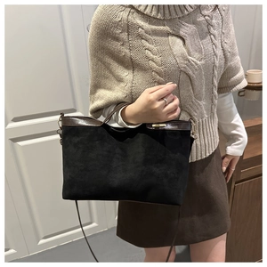 Detail of black suede tote bag with brown leather trim and golden metal hardware