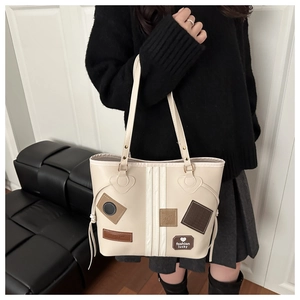 Detailed close-up of a cream tote bag with vintage patches and textured stitching