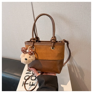Dettaglio di una borsa a secchiello marrone con ciondolo a forma di orsetto