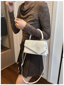 Detail of white crossbody bag featuring snake-patterned flap and smooth texture contrast