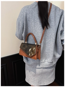 Detail of caramel leather handbag with faux snakeskin flap and golden metal hardware