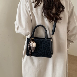 Sac à main léopard de style français avec anses noires porté par un mannequin en trench