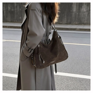 Borsa a secchiello in camoscio marrone con nappa e zip indossata da modella in trench grigio