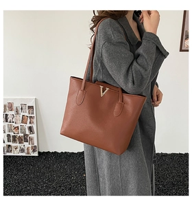 Close-up of large dark brown tote bag featuring gold V-shaped metal hardware and lychee texture