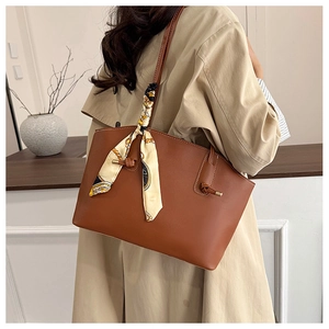 Brown leather tote bag with decorative silk scarf styled on a beige trench coat