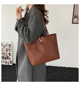 Detail view of brown pebbled leather tote bag with gold V-buckle on grey wool coat