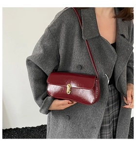 Detailed close-up of glossy burgundy baguette bag with a gold oval metal buckle