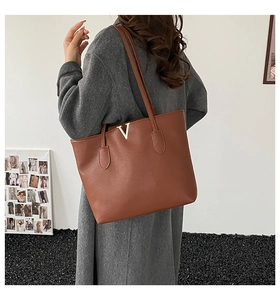 Detail of large brown tote bag with textured leather and gold V metal emblem
