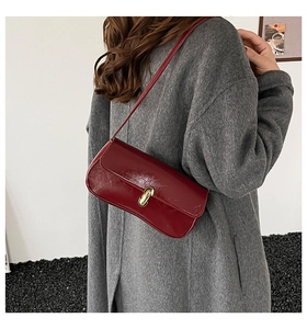 Detail of dark red underarm bag with gold capsule lock and glossy leather texture