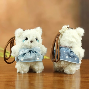 Detail of white plush teddy bear pendant with blue floral dress and pearl accents
