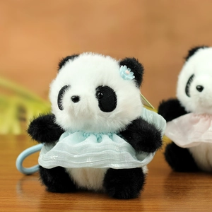 Dettaglio di portachiavi panda di peluche con vestiti blu chiaro e rosa su tavolo in legno