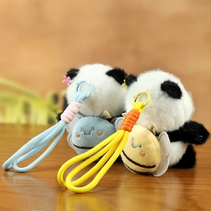 Close-up of plush panda keychain featuring small bee backpack on soft fabric texture