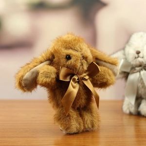 Close-up of soft plush bunny keychain with champagne satin bow on light wood background