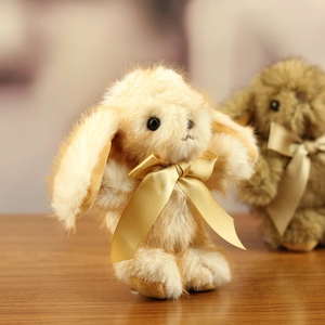 Close-up of fluffy cream plush bunny keychain with a golden satin ribbon and black eyes