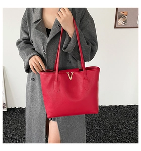 Close-up of red pebble leather tote bag with gold V hardware on a female shoulder