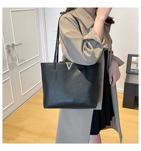 Detail of black pebbled leather tote bag featuring gold V-shaped metal hardware and strap