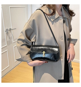 Detail of black glossy patent leather shoulder bag with a gold metal cylinder lock clasp