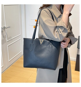 Detail of black pebbled leather tote bag with gold V-hardware on model in trench coat