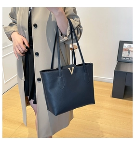 Detail of black large tote bag featuring gold V-shaped metal hardware and premium texture