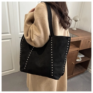 Détail du sac cabas noir mat avec rivets argentés porté par un mannequin en intérieur