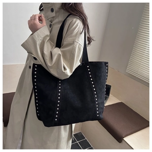 Details silberner Nieten an den Riemen der schwarzen Tragetasche mit beigem Trenchcoat