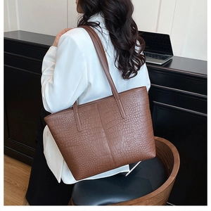 Detail of a brown tote bag with crocodile texture worn by a model in office setting
