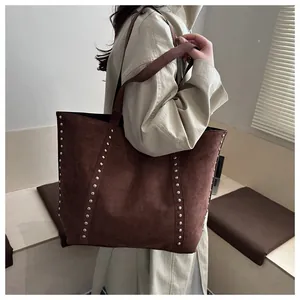 Détail d'un grand sac cabas en daim marron avec des rivets argentés et de longues bandoulières