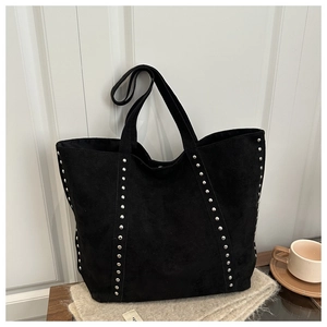 Detailaufnahme der schwarzen Wildleder-Tote-Bag mit Nieten auf einem Holztisch mit Kaffee