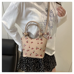 Dettaglio di una borsa a secchiello beige con stampe di ciliegie e ciondolo floreale