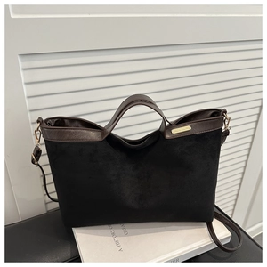 Detail of matte black tote bag with brown leather handles and gold metal hardware hooks