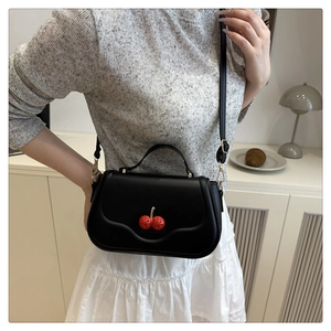 Detail of black leather handbag with 3D red cherry accents and adjustable strap