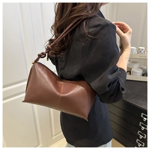 Detail of brown leather underarm bag with knot strap and matte texture on model