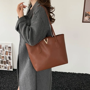 Brown leather tote bag with V-shaped gold metal detail shown on an elegant model